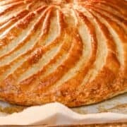 A round, golden brown puffed up cake on brown parchment paper.