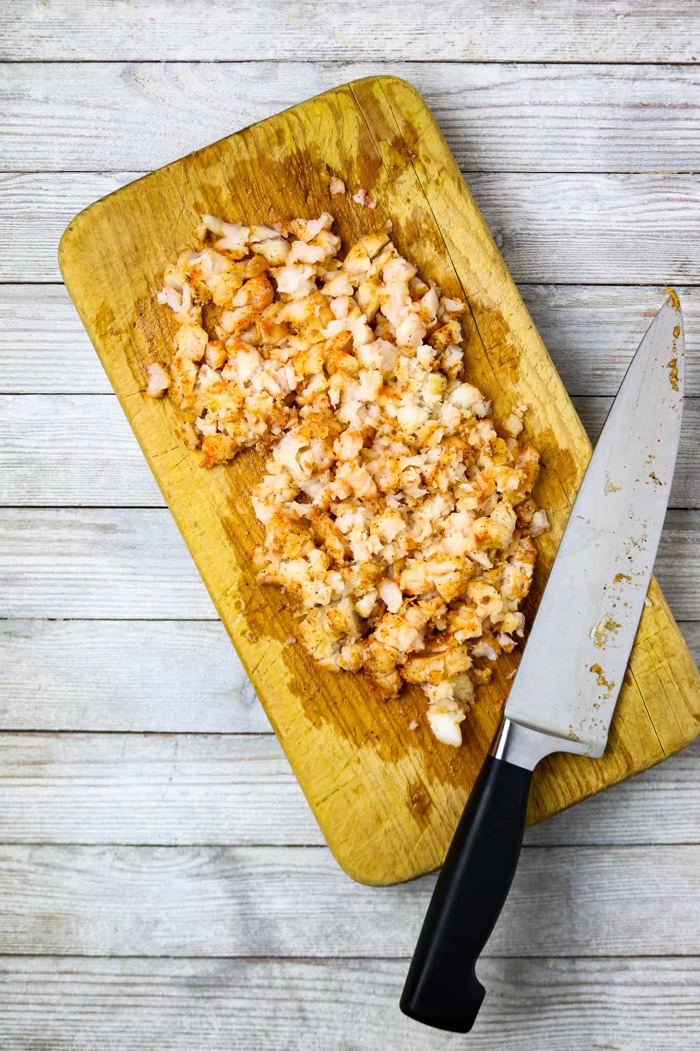 Chopped shrimp on a cutting board with a knife.