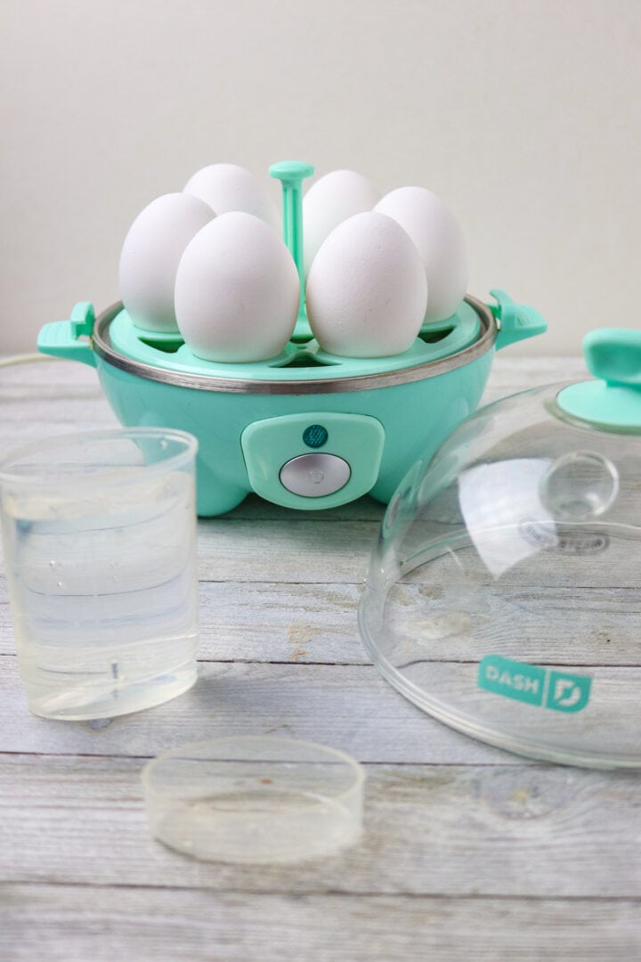 An electric egg cooker with white eggs in it.