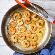 A large silver skillet with tongs tossing sautéed shrimp.
