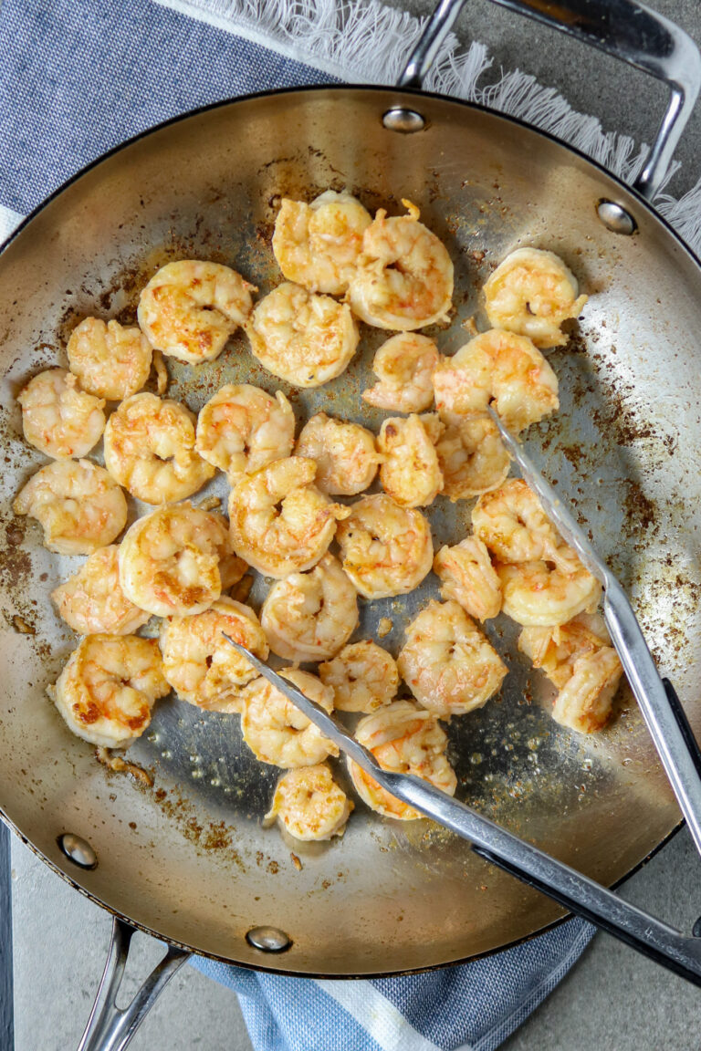 A large silver skillet with tongs tossing sautéed shrimp.