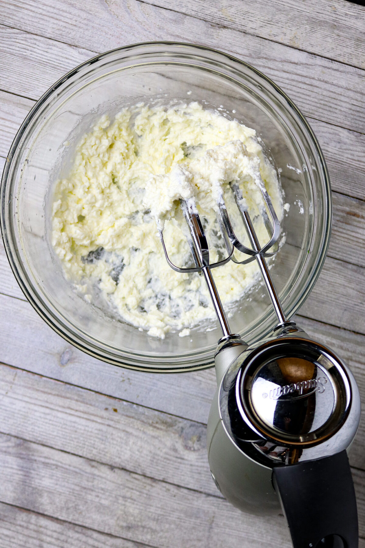 A mixer with beaters in a bowl of mixed cream cheese.