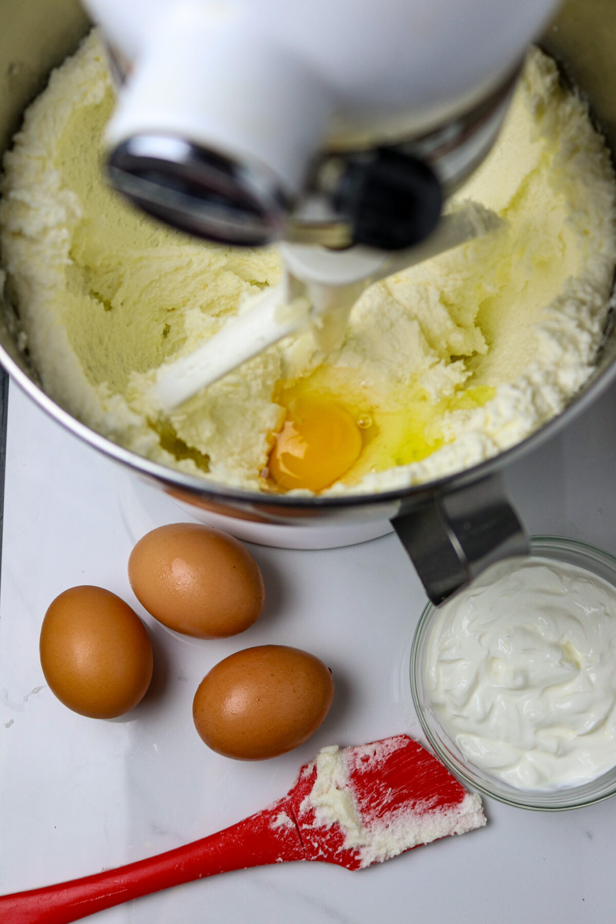 Three eggs beside a stand mixer with cake batter in the bowl.