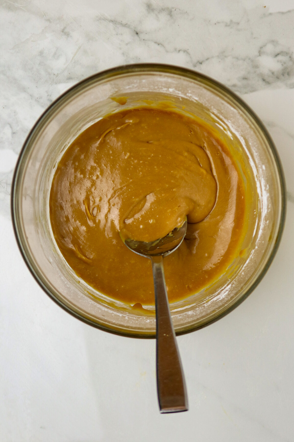 A bowl of caramel glaze in a glass bowl with a spoon in it.