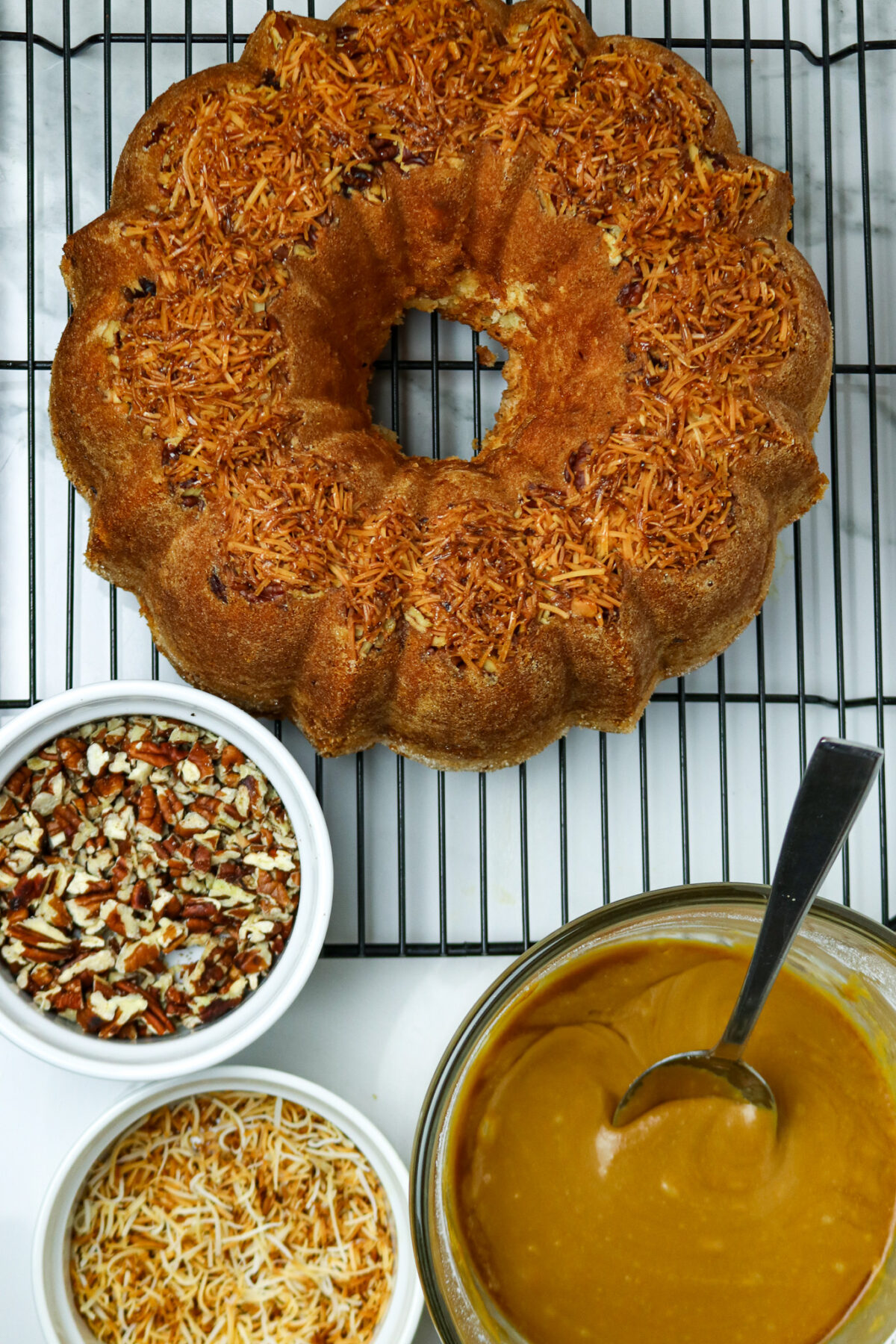 A bundt cake with a bowl of pecans and a bowl of glaze next to it.