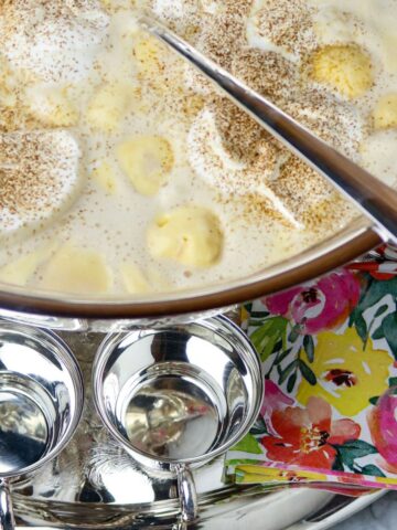 A large. silver punch bowl filled with punch on a silver platter with silver punch cups.