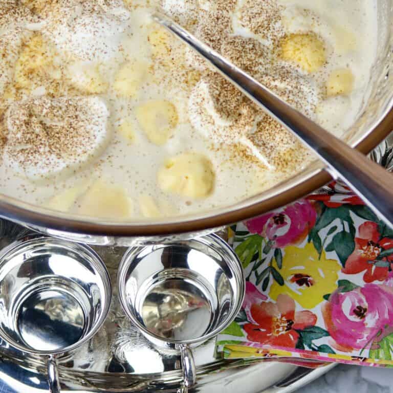 A large. silver punch bowl filled with punch on a silver platter with silver punch cups.