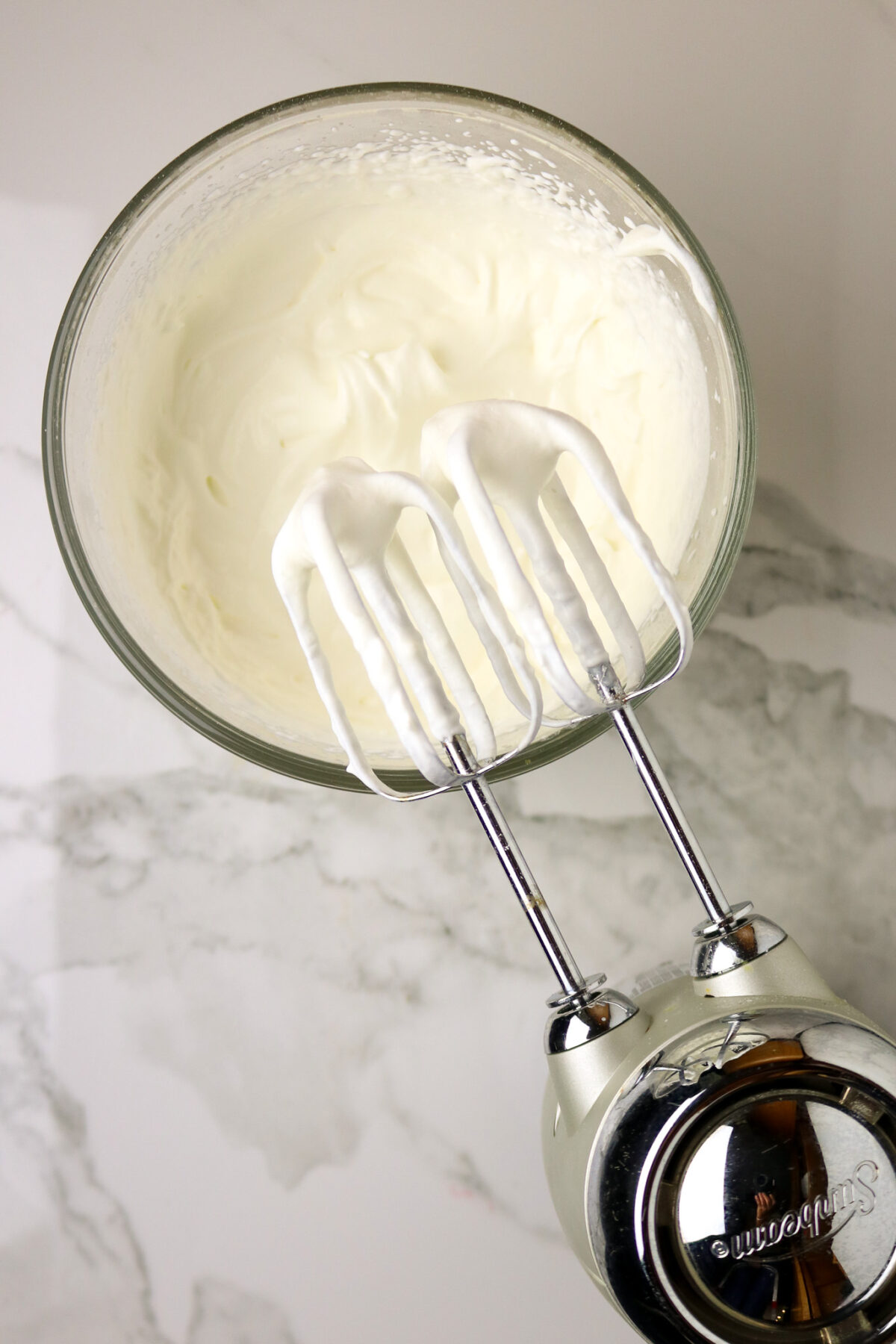 A bowl of whipped cream with and electric mixer beaters over the bowl.