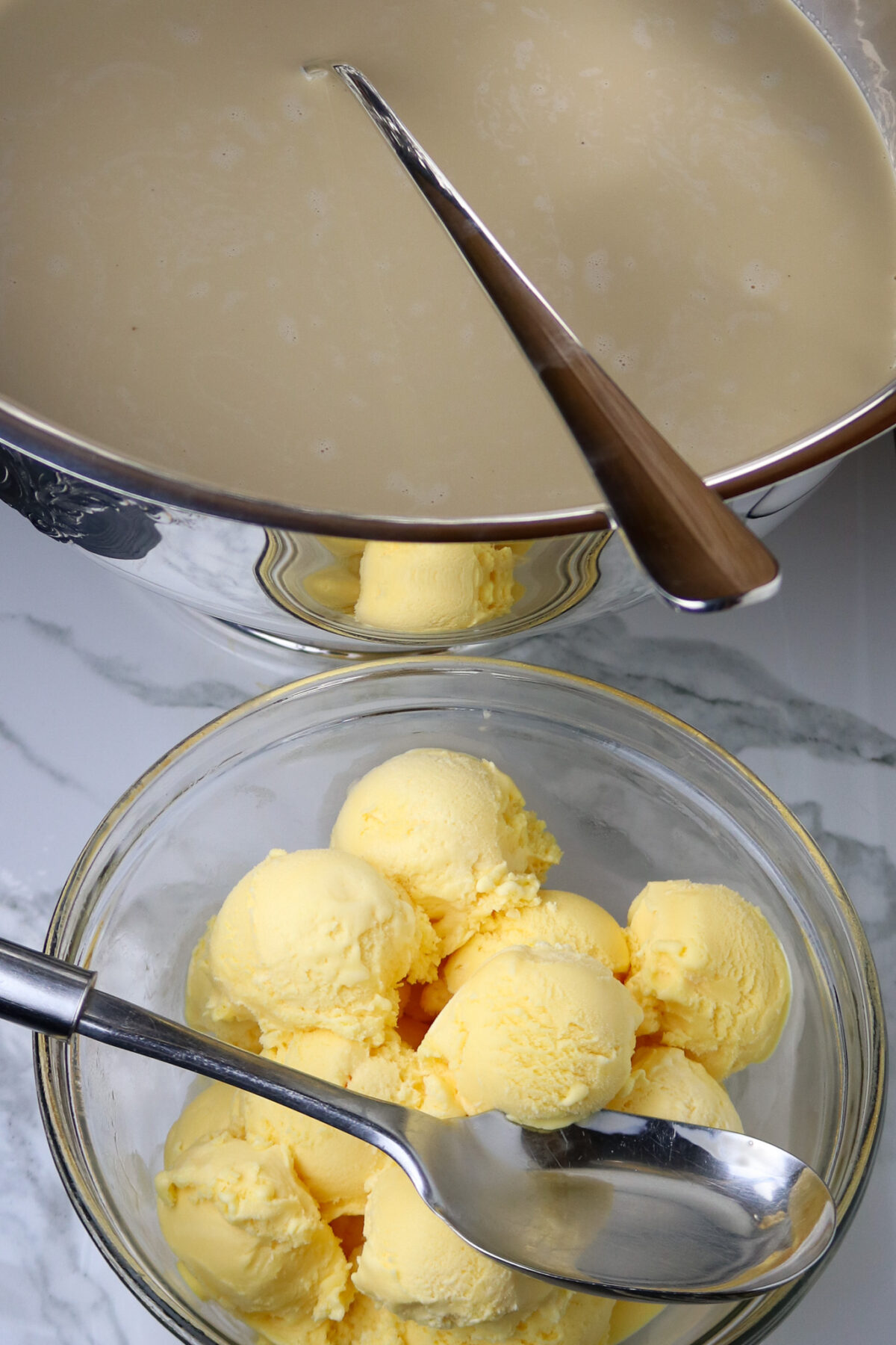 A bowl of ice cream scoops next to a punch bowl with a silver ladle.