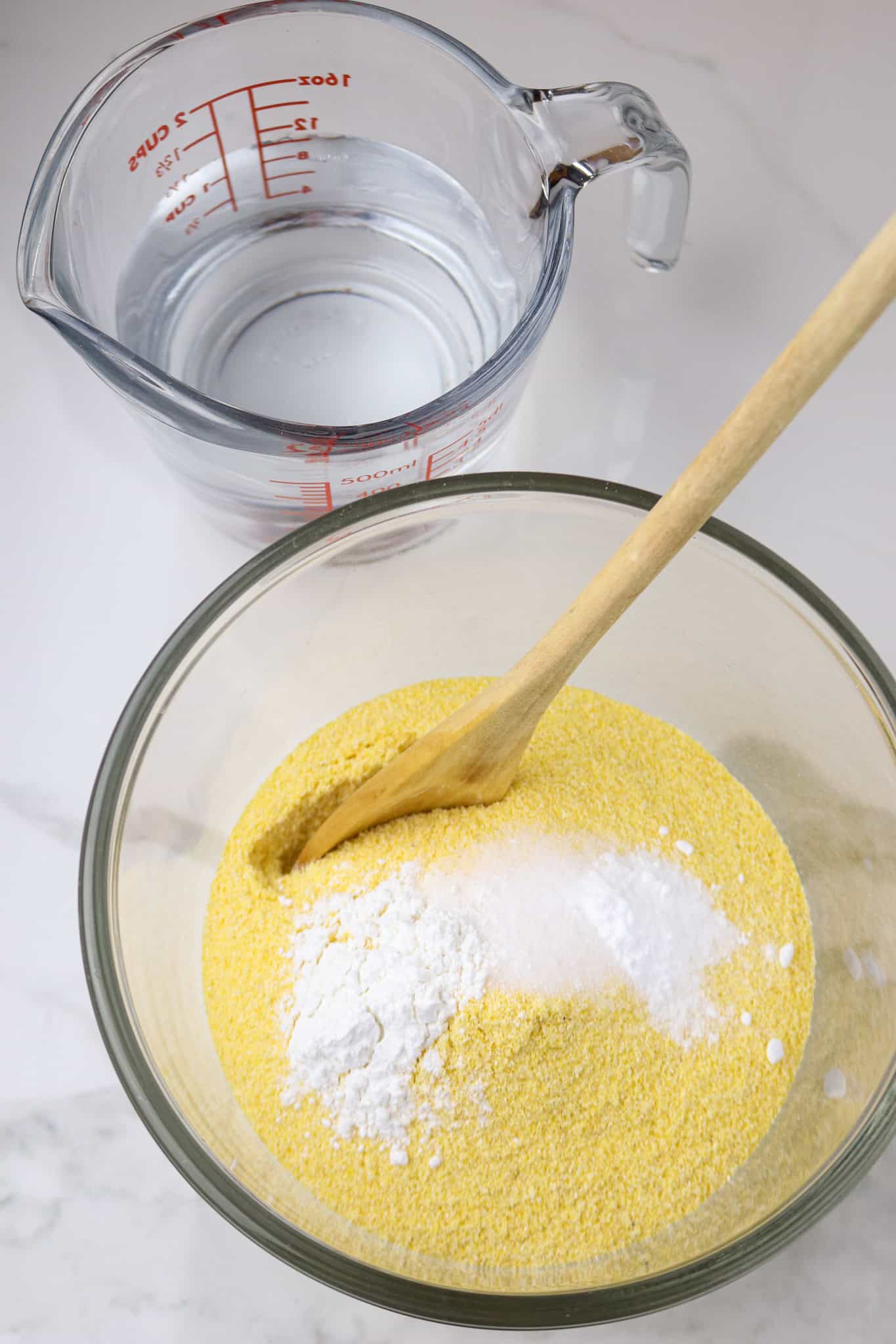 A glass bowl with corn meal and a wooden spoon in it.