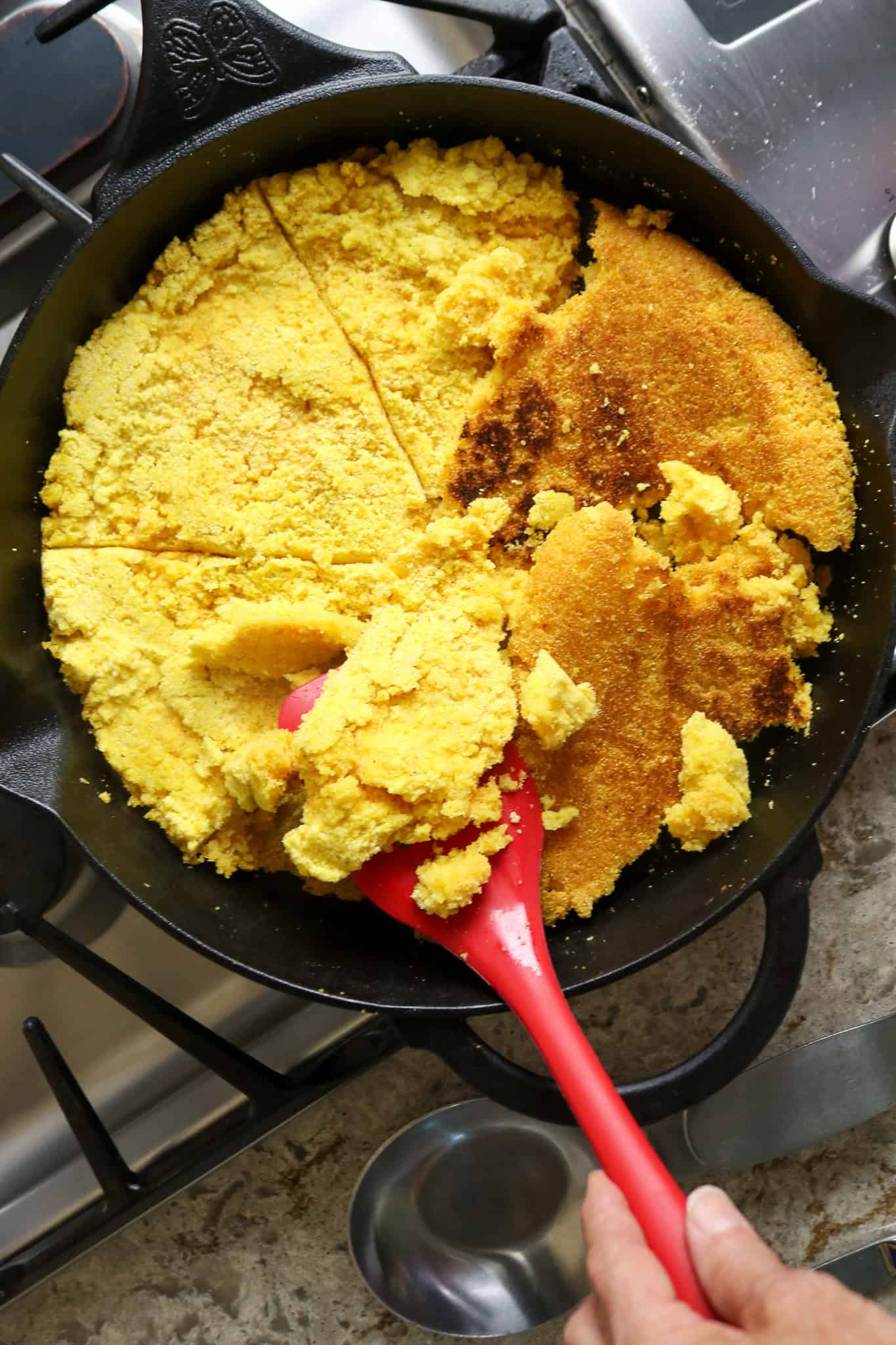 A red spatula turning over cooked corn bread crumbles.