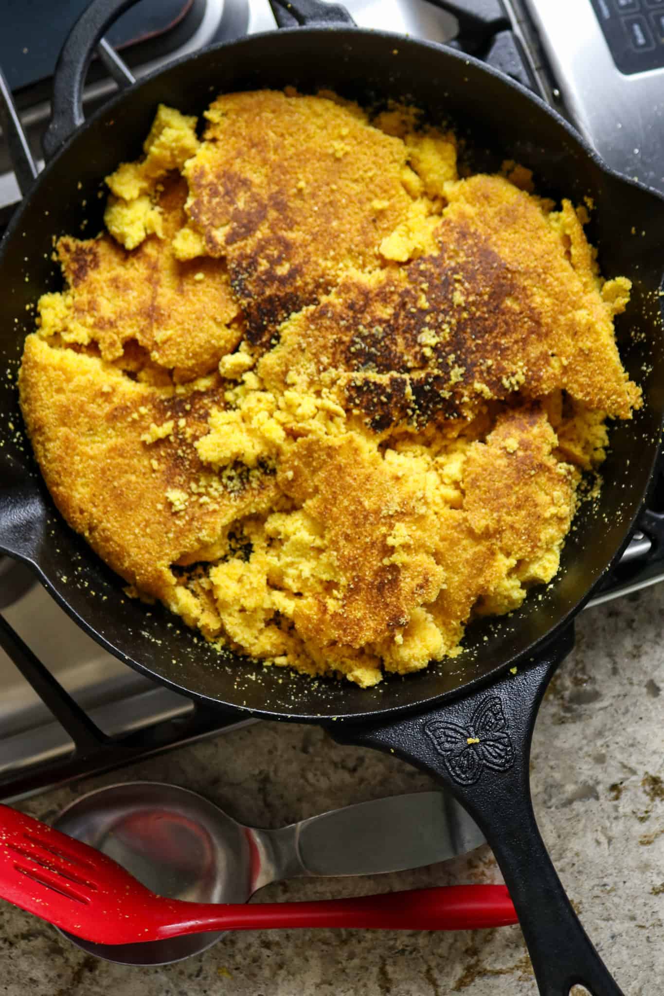 Golden crumbled couche couche in a black iron skillet.