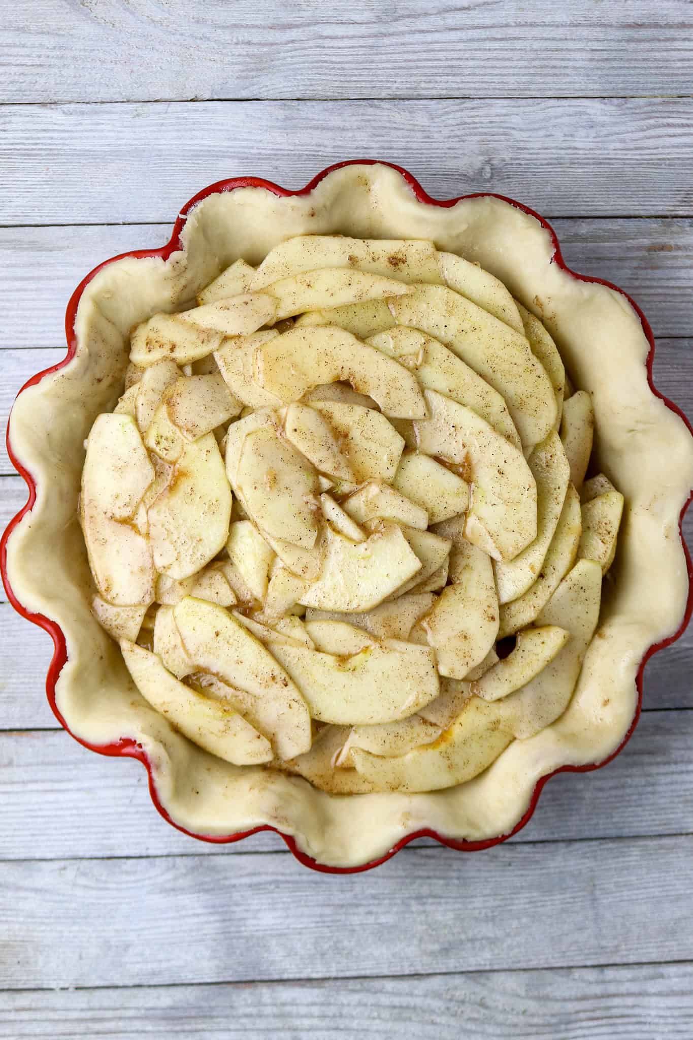 Sliced apples covered in cinnamon and butter in a red scolloped edge pie dish for a paper bag French apple pie.