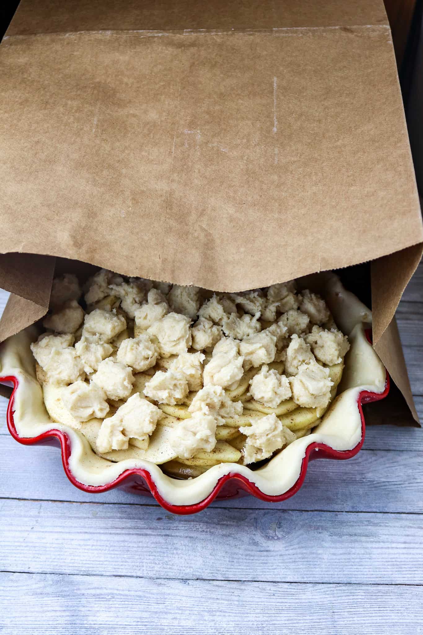 A pre-baked French apple pie topped with dollops of batter in a brown paper bag.