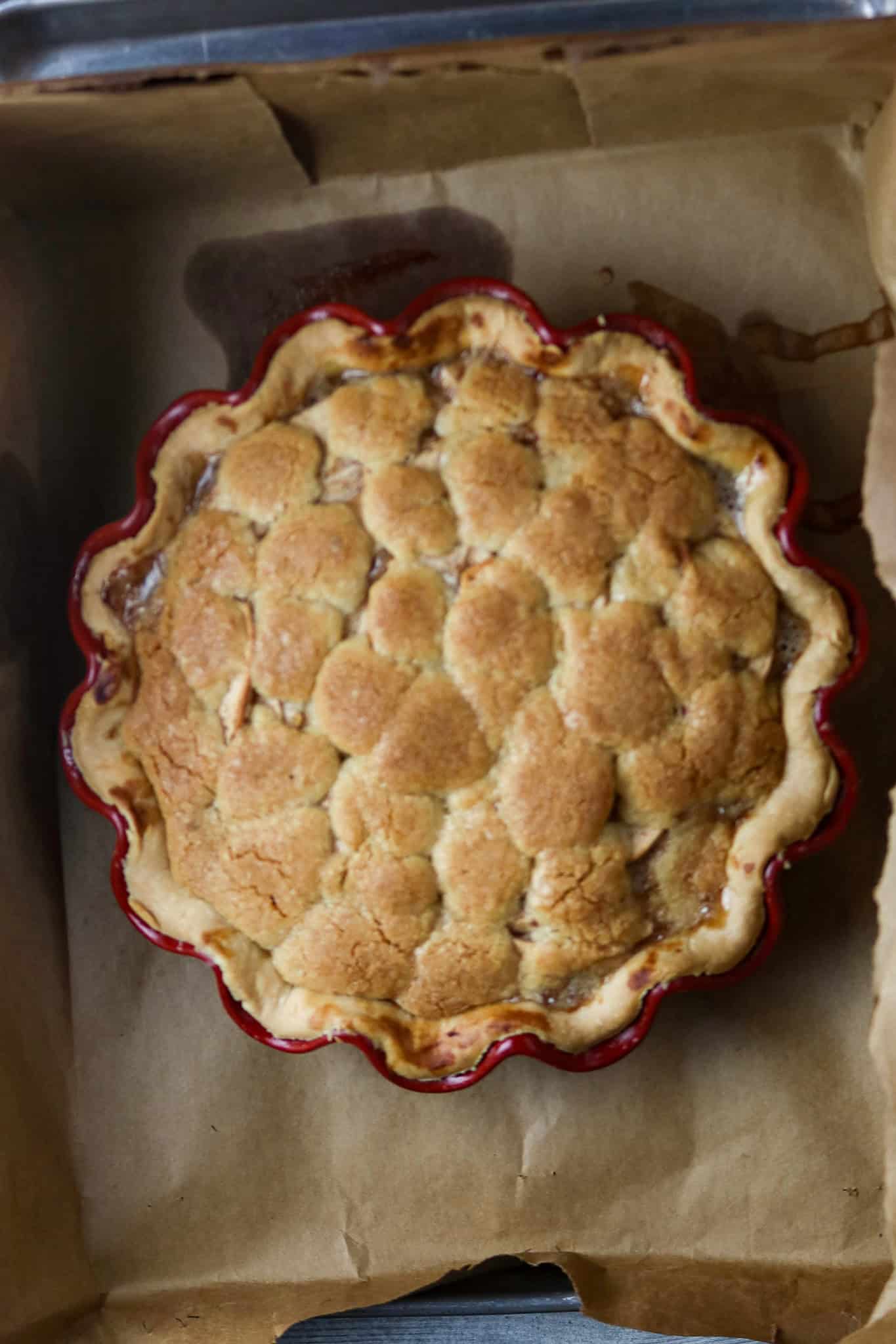 A French apple pie covered in a golden topping in a scalloped pie dish on a paper bag.