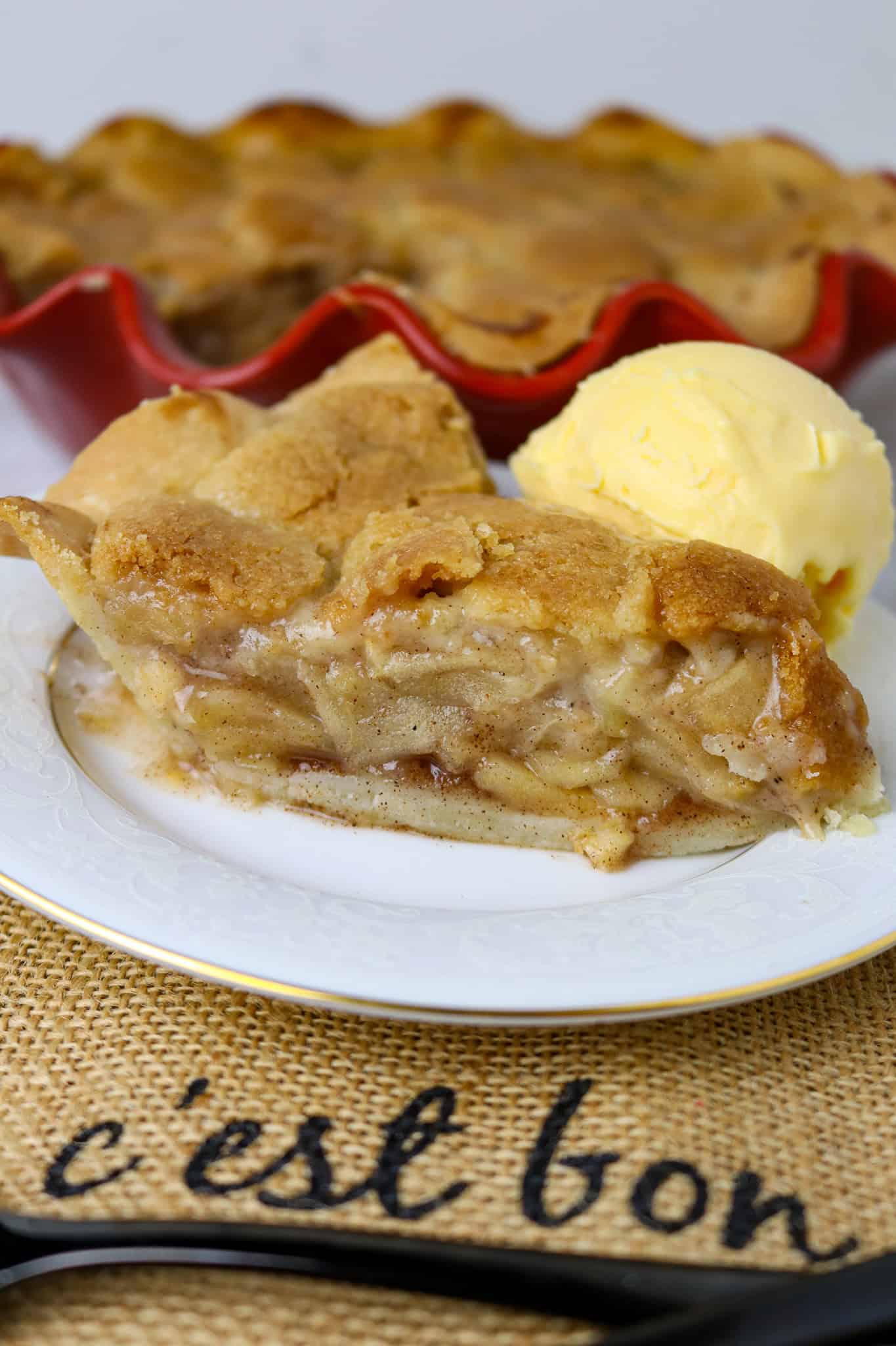 A cut piece of apple pie on a white plate with a scoop of ice cream.