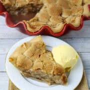A cut piece of apple pie on a white plate with a scoop of ice cream.