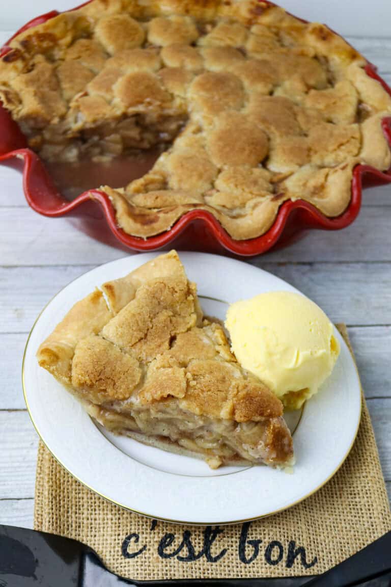 A cut piece of apple pie on a white plate with a scoop of ice cream.