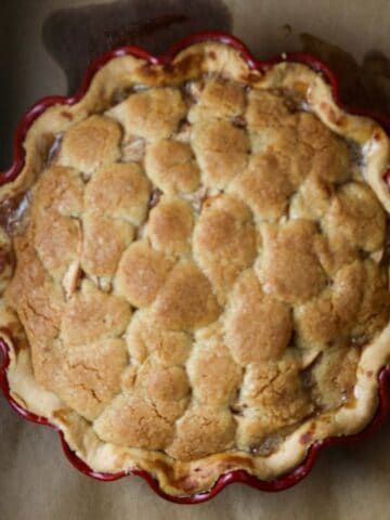 A pie covered in a golden topping in a scalloped pie dish on a papre bag.