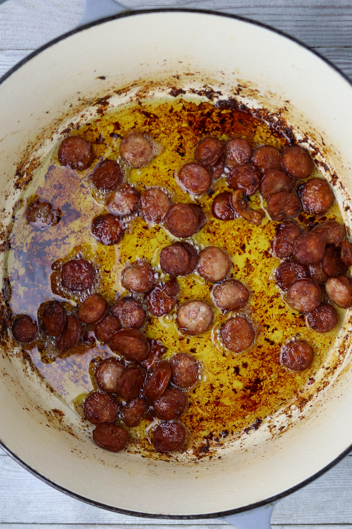 Browned sausage sliced cooked in oil in a Dutch oven.