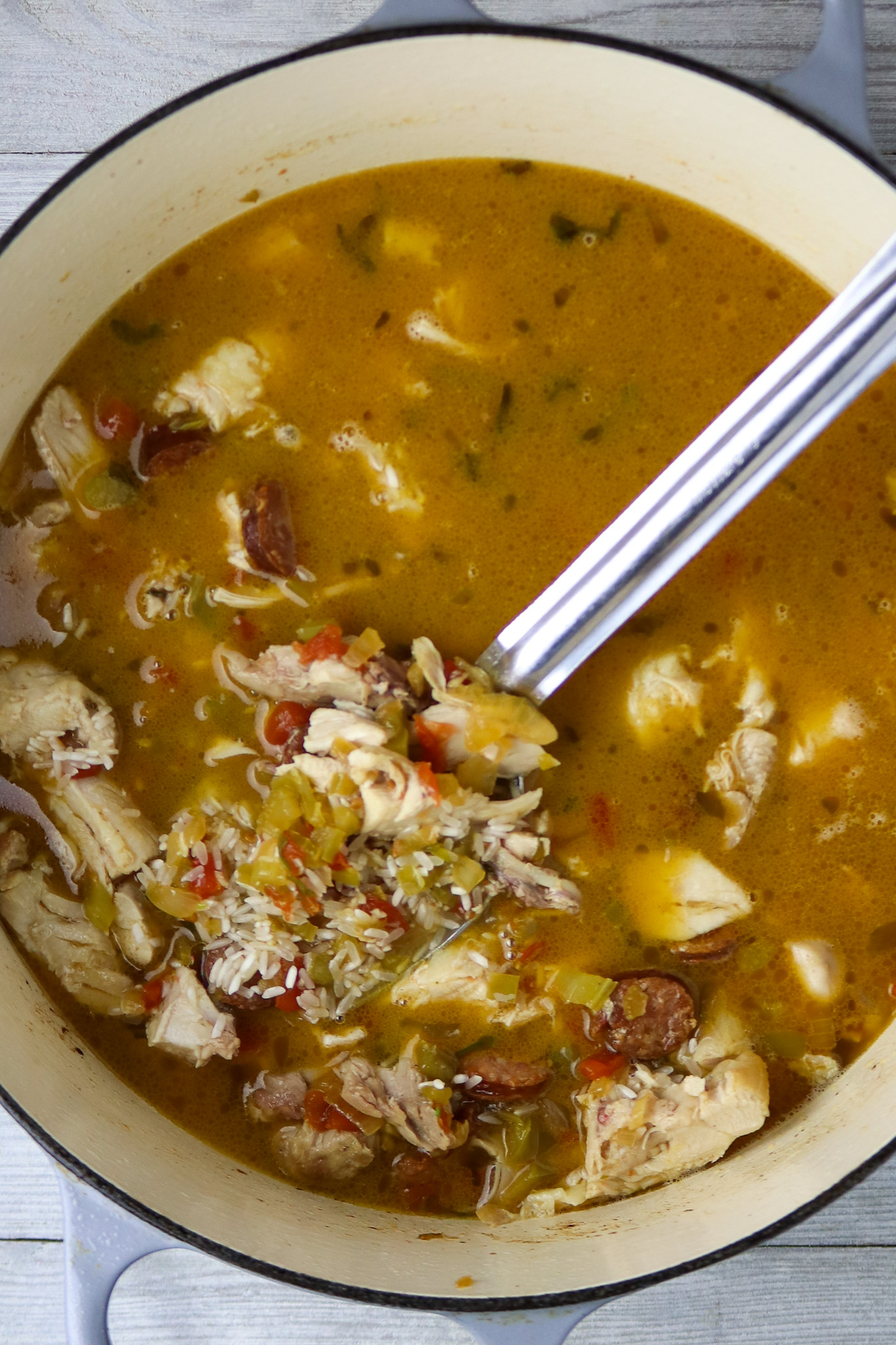 A pot of chicken and shrimp jambalaya in a Dutch oven pot with a long-handled silver spoon in it.