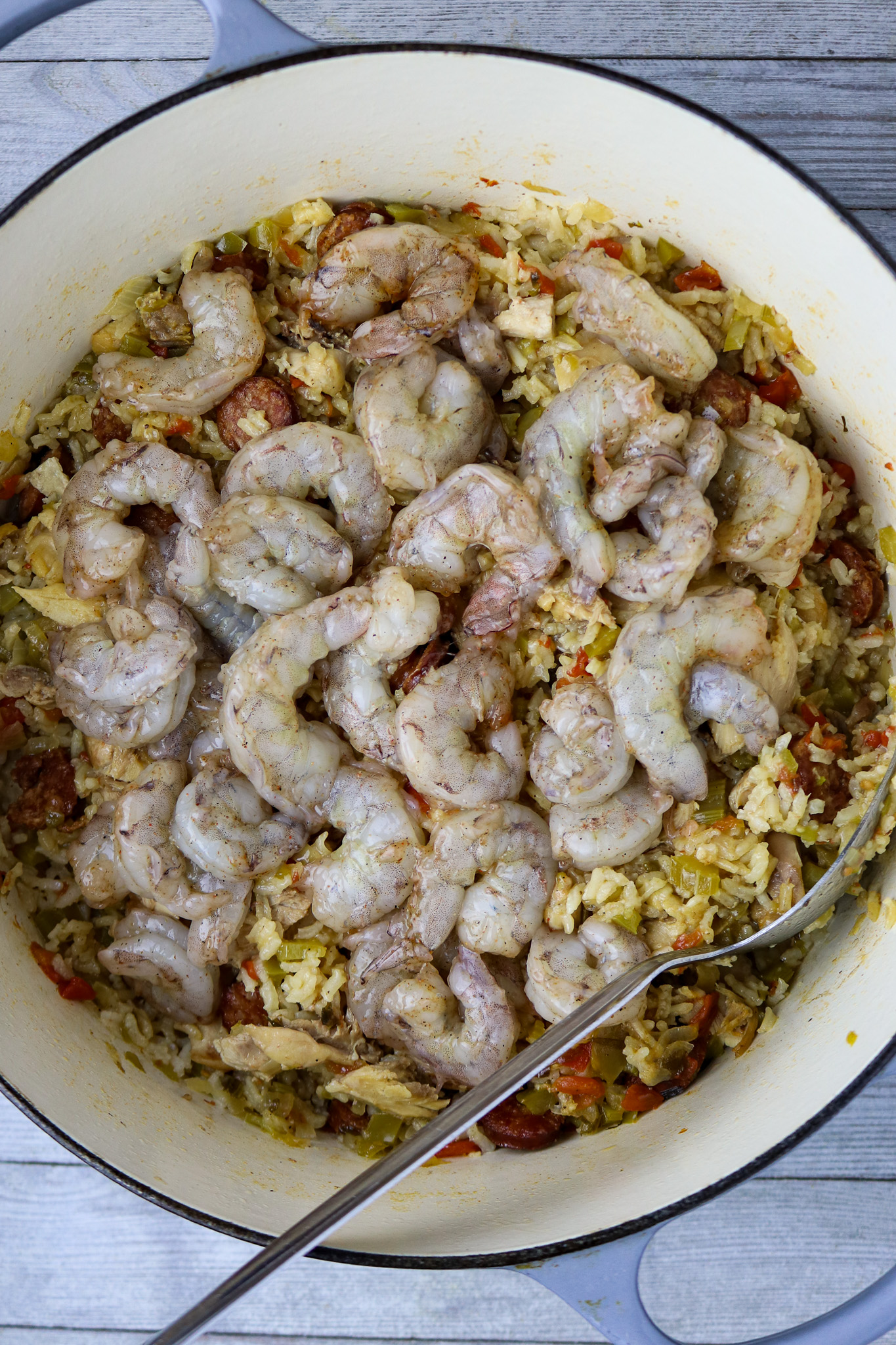 A pot of uncooked jambalaya with raw shrimp on top..