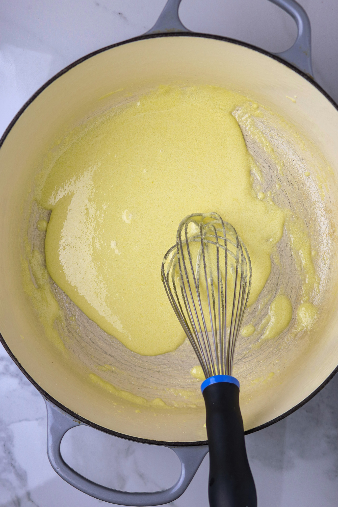 A whisk in a large dutch oven pot over a lemon colored whipped egg and sugar mixture.