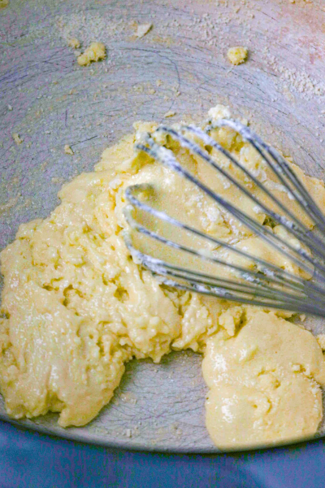 A whisk in a thick mixture of egg, sugar, and cornstarch in a pot.