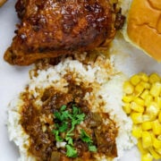 A plate of chicken sauce piquant, rice and gravy, corn and a roll.