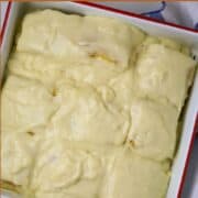 A square pan with a red trim filled with cake squared and covered with custard.