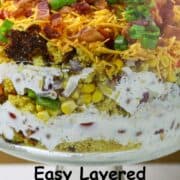 A large glass bowl of layers of salad ingredients of peppers, corn, onion, bacon, cheese, and cornbread.