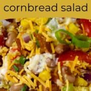 A large glass bowl of layers of salad ingredients of peppers, corn, onion, bacon, cheese, and cornbread.