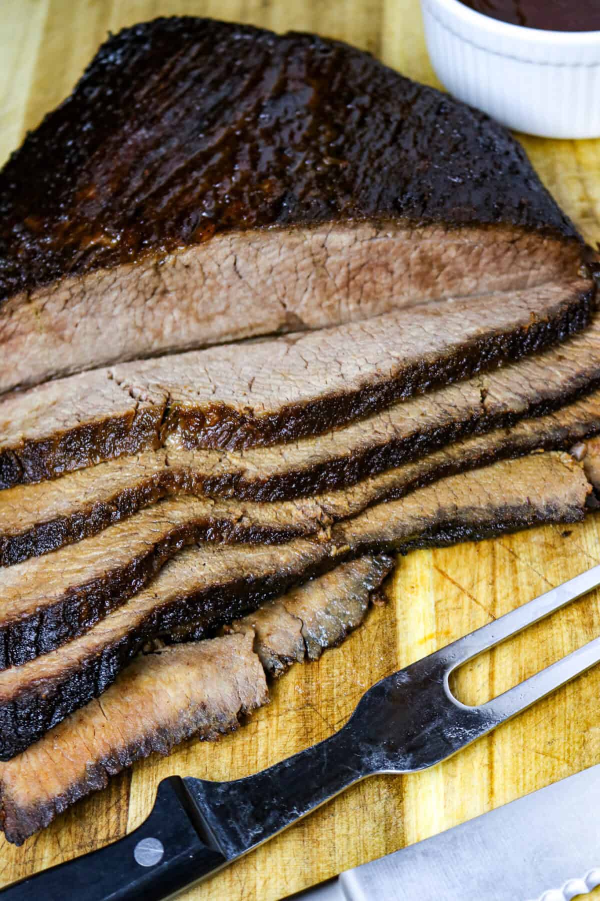 A sliced brisket on a board with a long fork next to it.