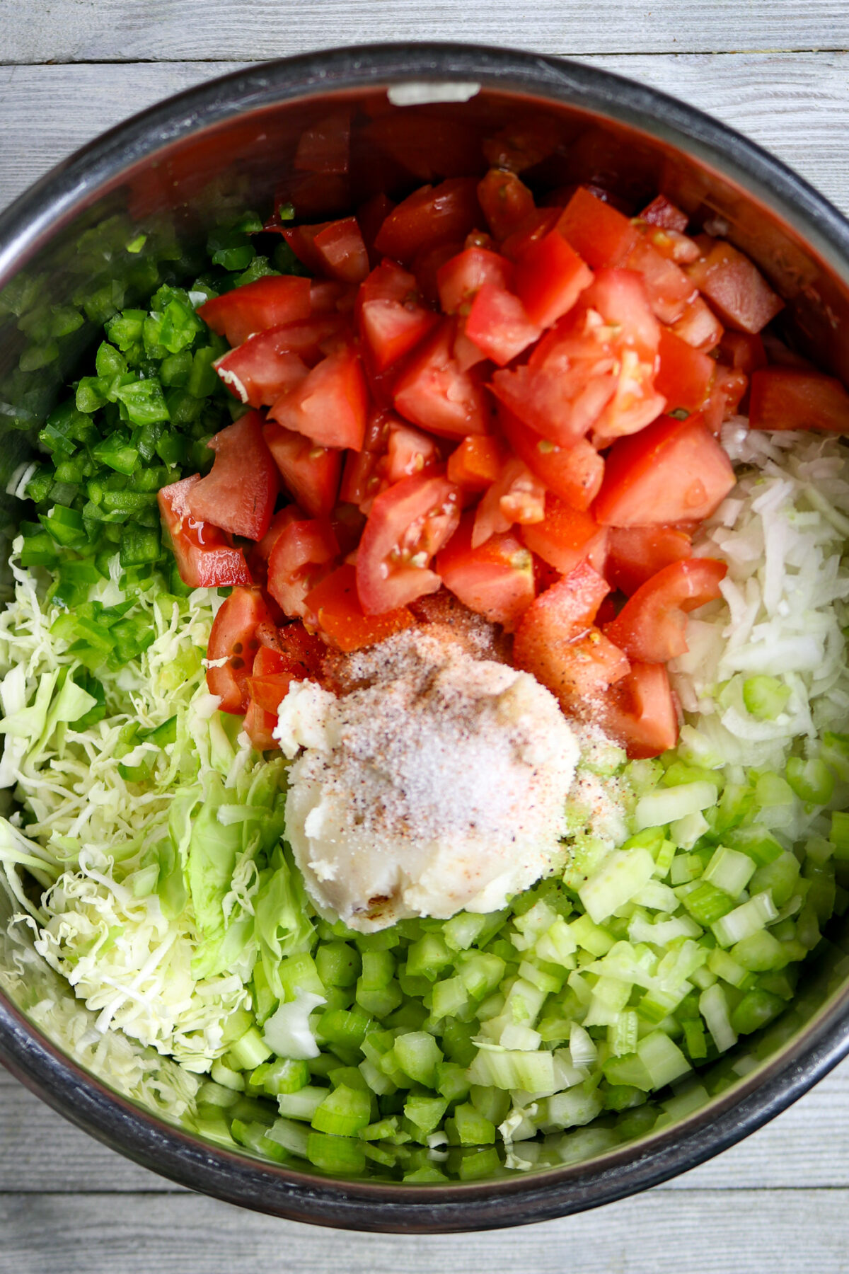 Raw ingredients of tomatoes, cabbag, onion, celery, anbd bell peppers in a pot.
