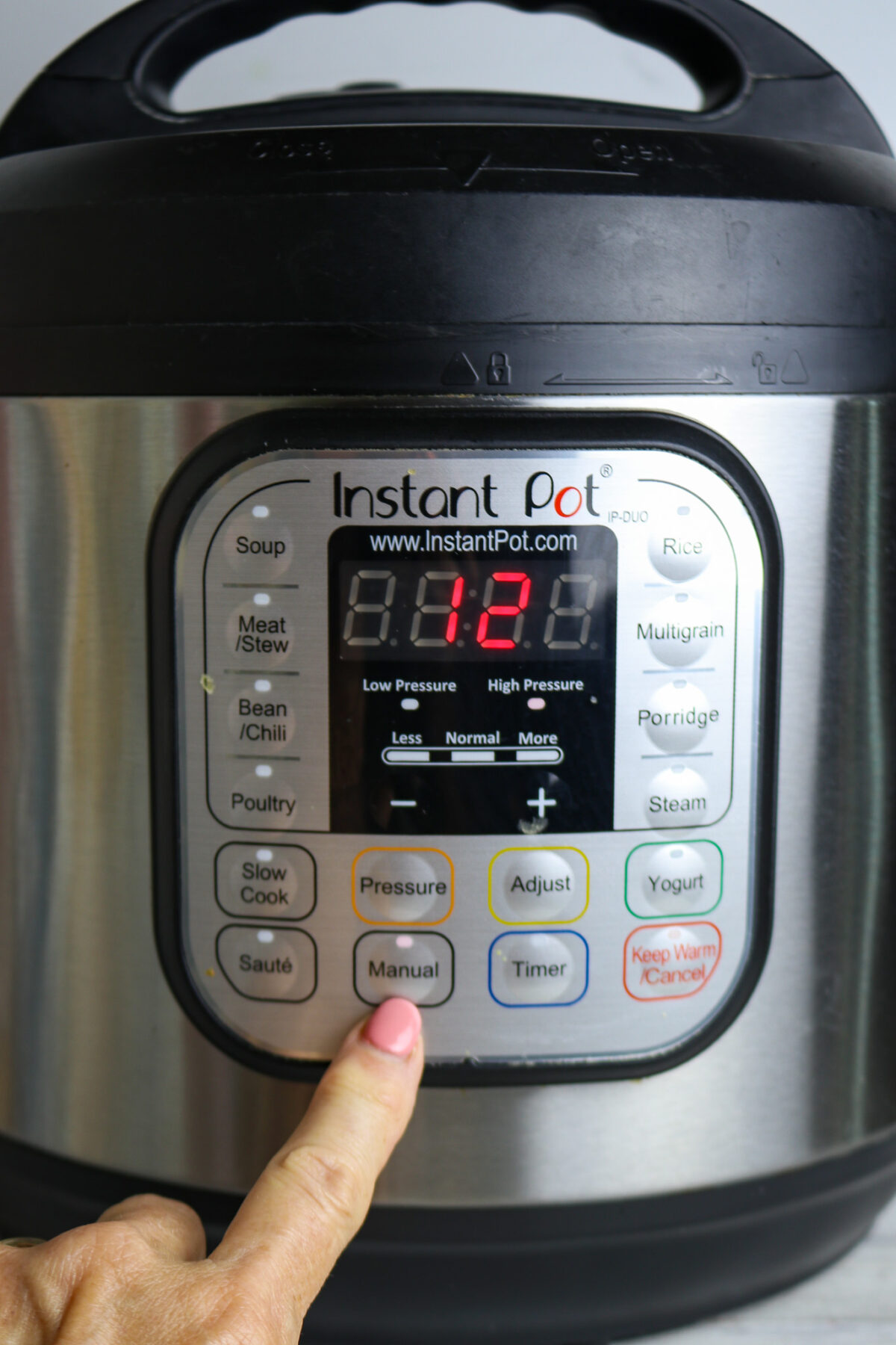 An Instant Pot with a finger pointing to the manual button.