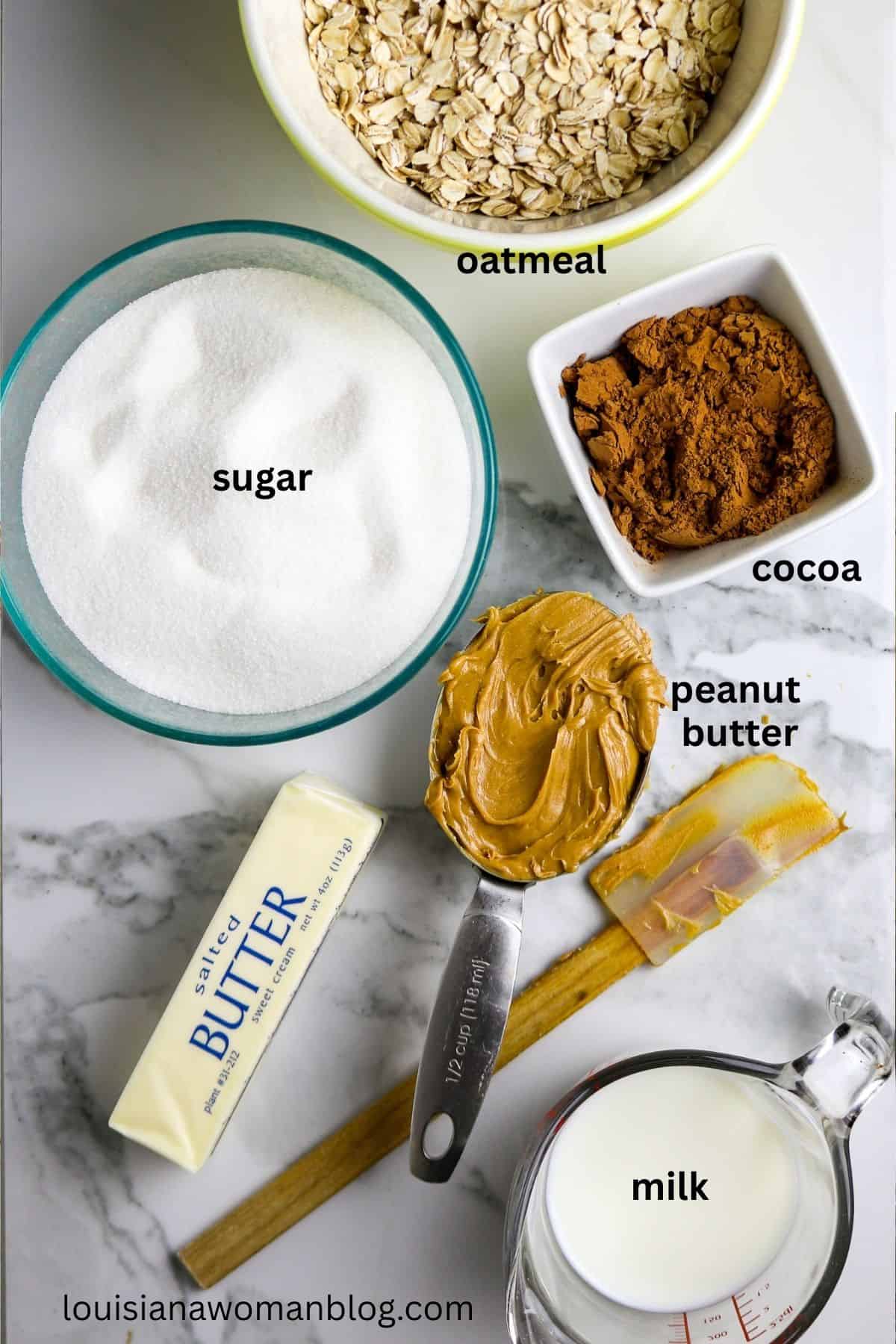 Individual ingredients of sugar, butter, cocoa powder, peanut butter, milk, and oatmeal on a marble counter.