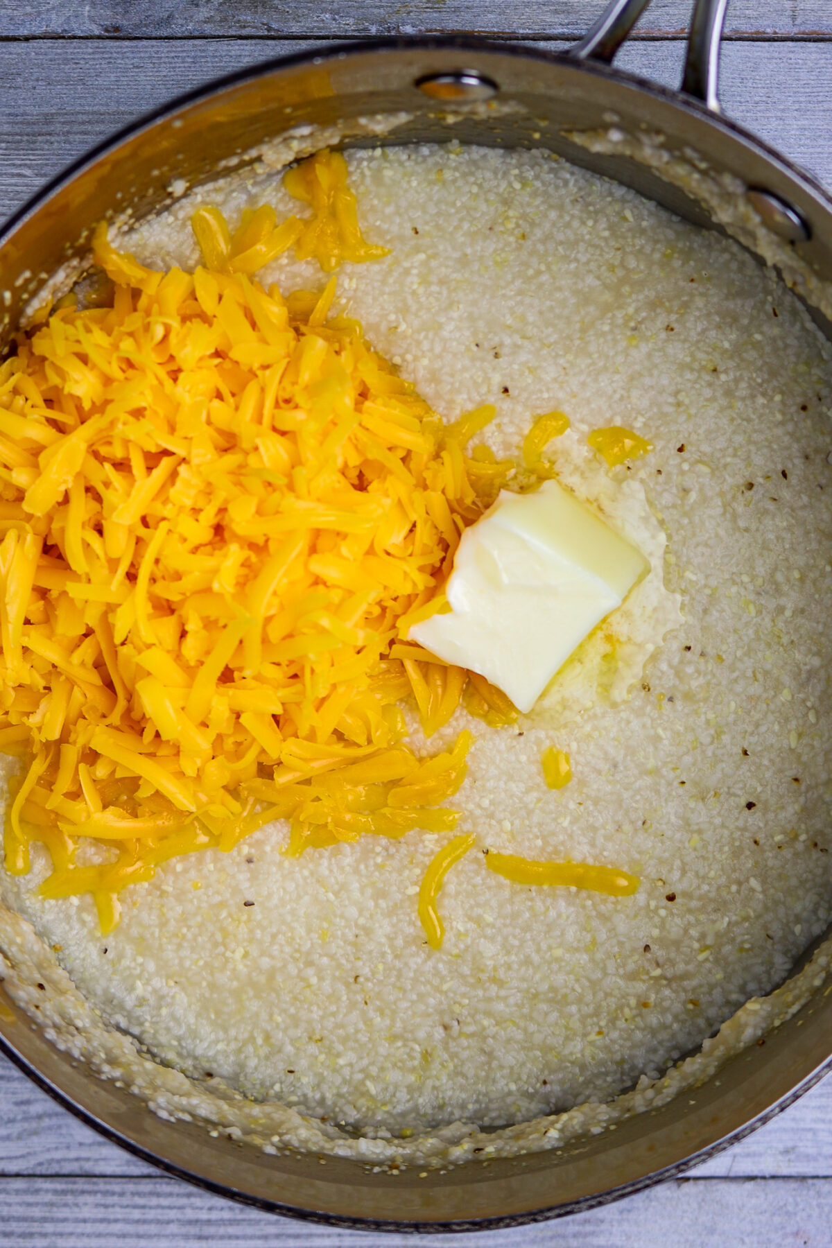 A pot of cooked grits with grated cheese and a pat of butter to go in Cajun Shrimp and Grits Recipe with Andouille Sausage.