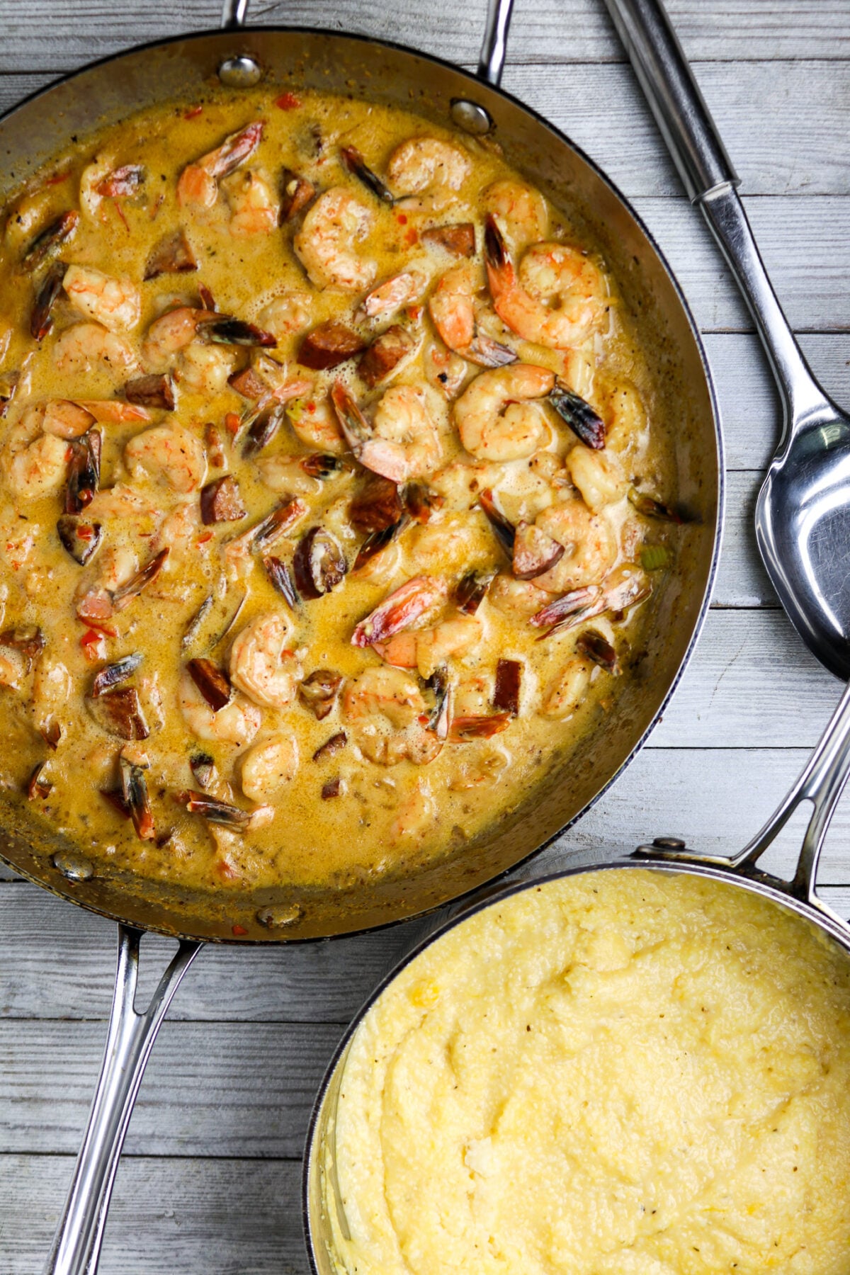 A pan of shrimp in a cream sauce with a pot of grits beside it for Cajun Shrimp and Grits Recipe with Andouille Sausage.