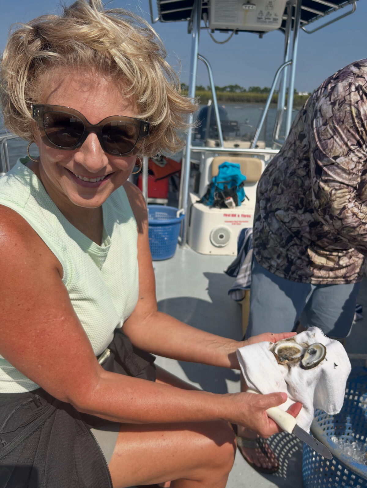 A lady sitting in a boat holding an opened oyster shell.