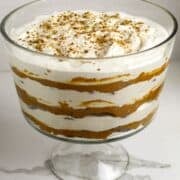 A footed glass dish with 6 layers of cookies, pumpkin, and whipped cream with cookie sprinkles on top.