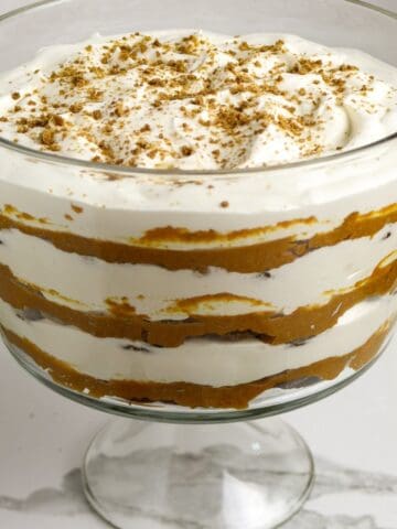 A footed glass dish with 6 layers of cookies, pumpkin, and whipped cream with cookie sprinkles on top.
