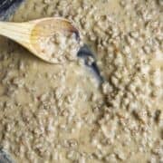 A black cast-iron skillet with meat and white sauce and a wooden spoon.