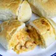 A plateful of crawfish pistolettes with one roll front and center, cut in half with cheesy crawfish sauce oozing out..