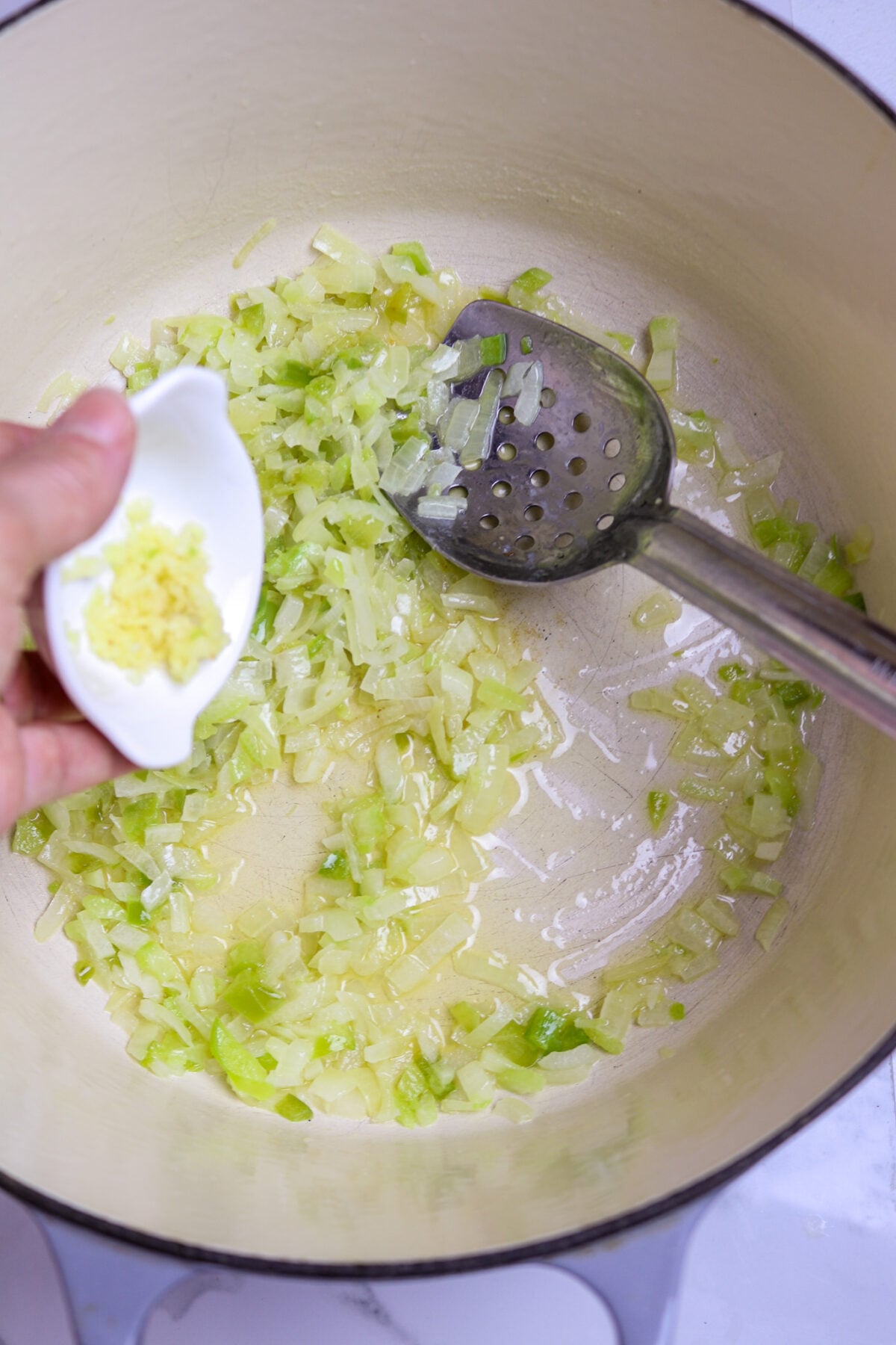 A small bowl of garlic poured into a pot of onions, celery, and green pepper for crawfish pistolettes.