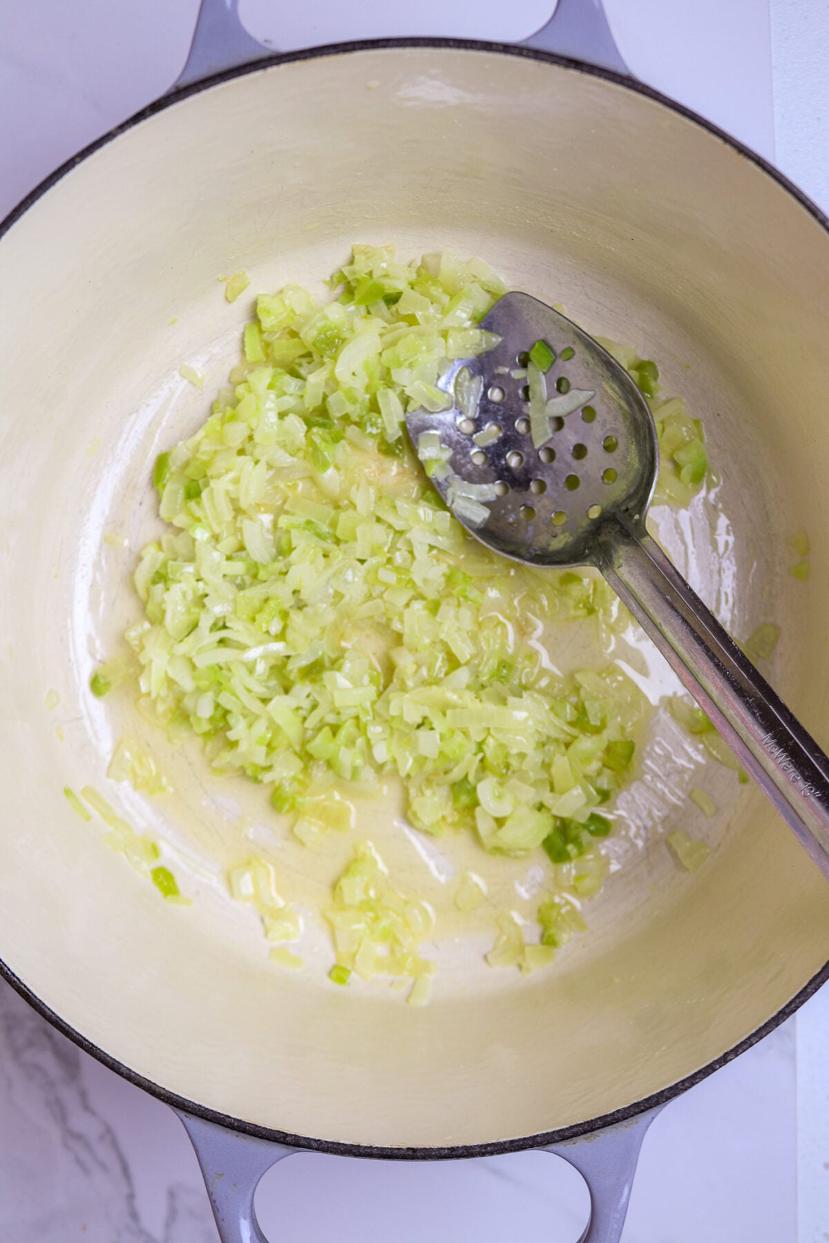 A long silver spoon in a pot of onions celery, and green bell pepper for crawfish pistolettes recipe.
