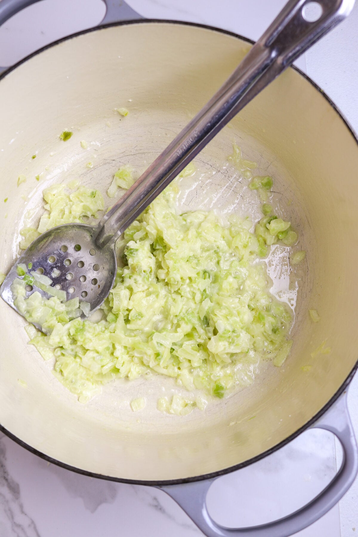 A long silver spoon in a pot of onions celery, and green bell pepper with cornstarch.