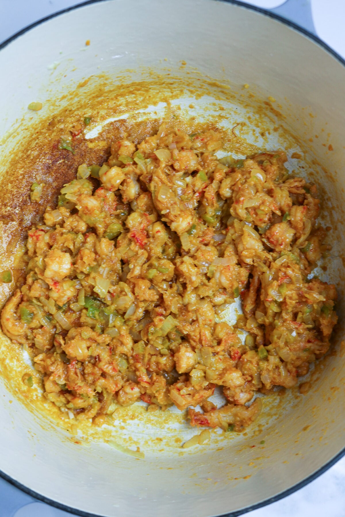 A thick sauce with crawfish tails in a large white pot.