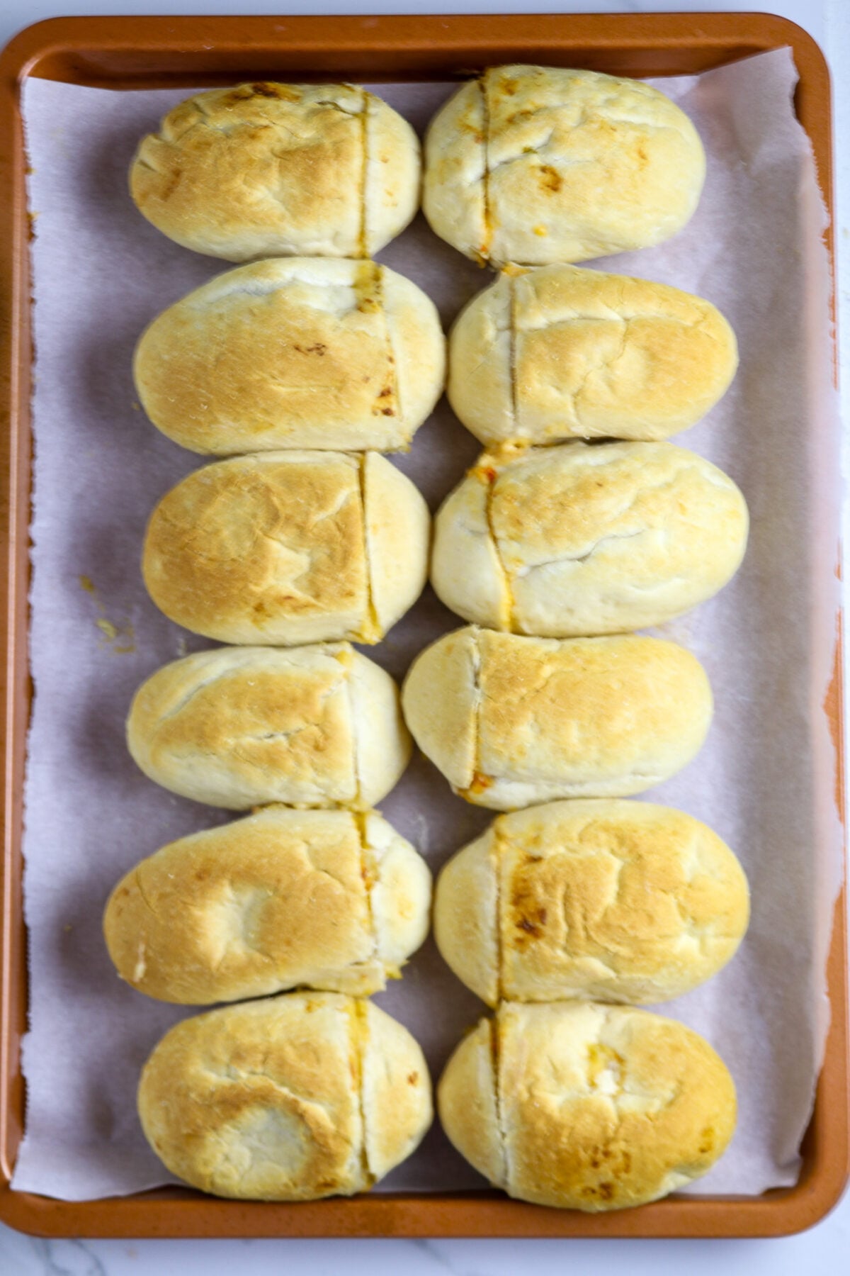 Two rows of six small browned French bread rolls on a cookie sheet lined with parchment paper.