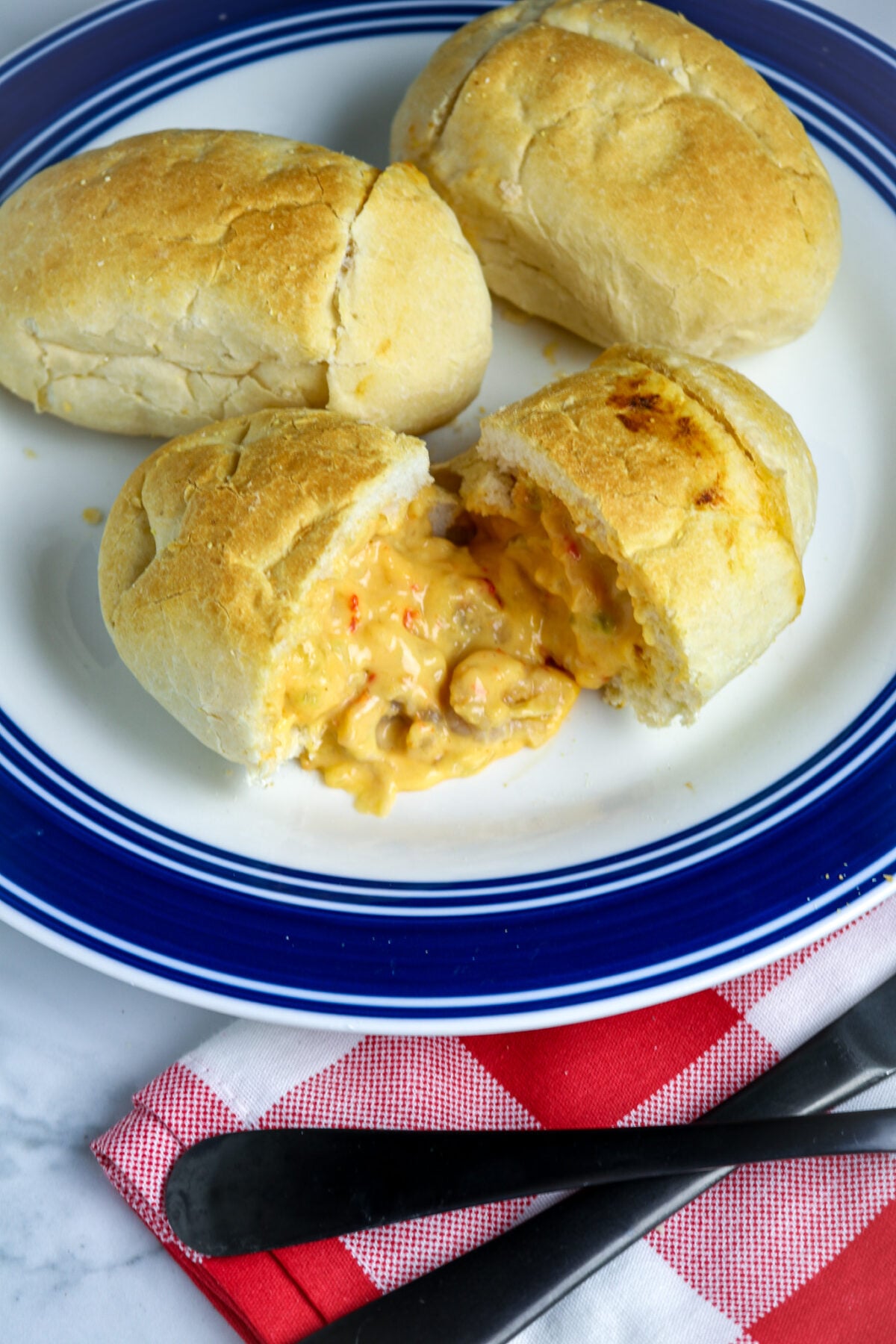 A white plate with a blue rim with 3 pistolettes and one cut in half with crawfish sauce pouring out.