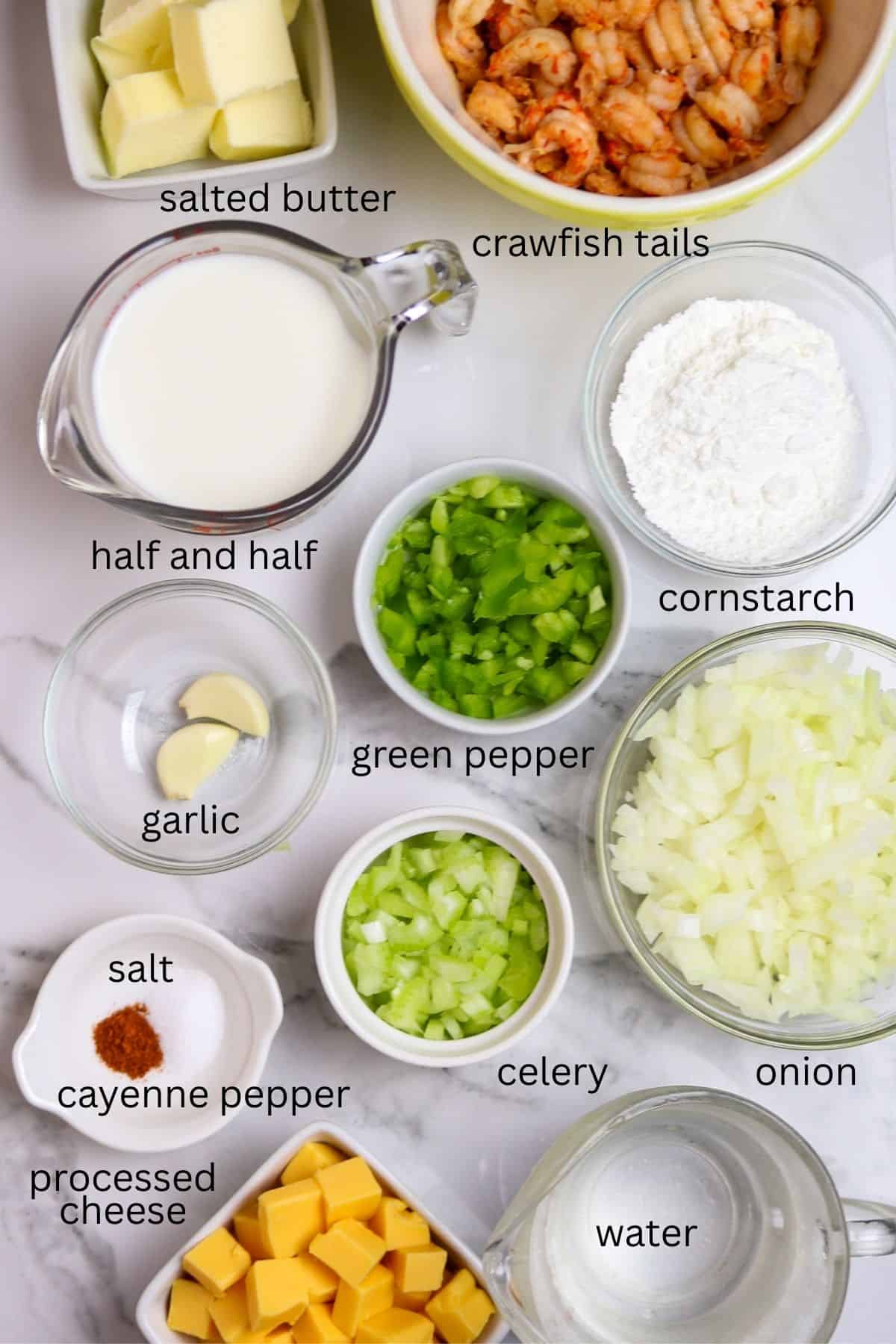 Ingredients of crawfish, onions, garlic, green pepper, celery, butter, cream, cornstarch, and seasoning in individual containers on a white and gray marble countertop.